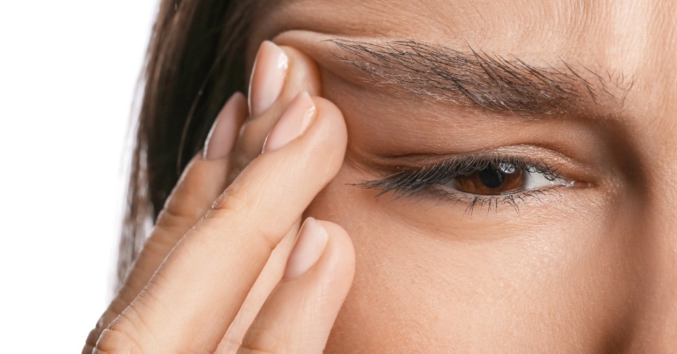 Close de mulher tocando a região dos olhos para ilustrar o incômodo do tremor de pálpebras.