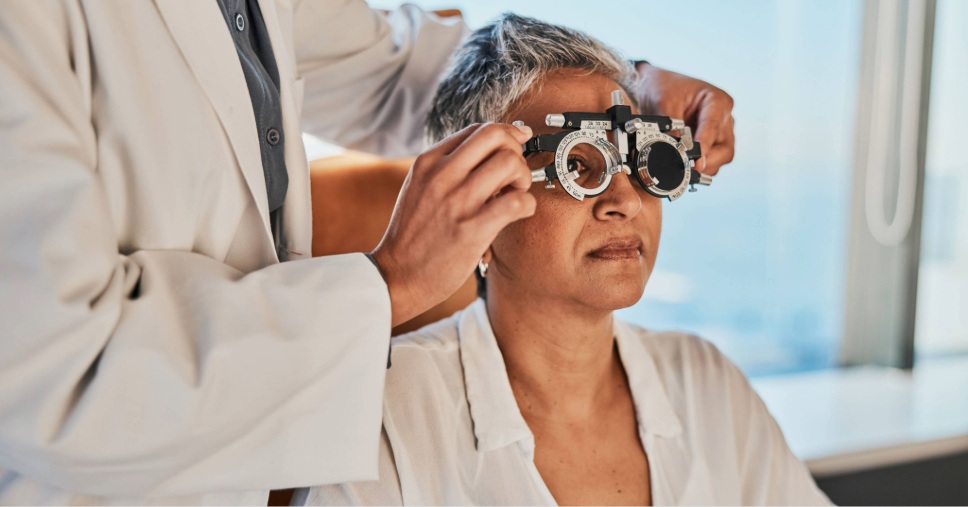 Oftalmologista ajusta óculos de teste em paciente de cabelos grisalhos para saúde ocular preventiva.